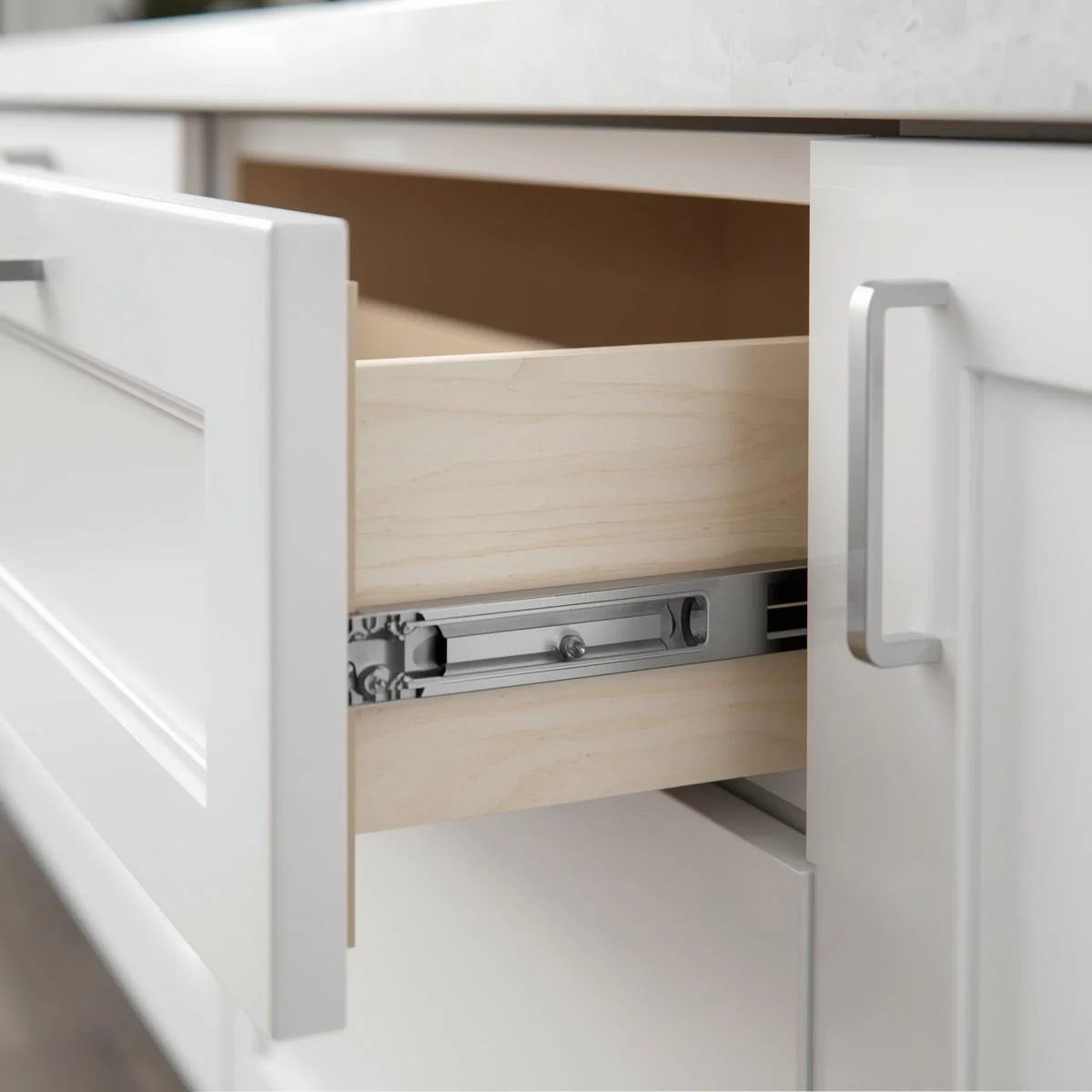 Otwarta biała szuflada kuchenna z widoczną boczną prowadnicą metalową i drewnianym bokiem szuflady